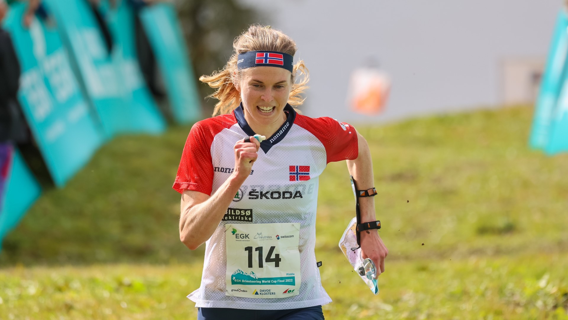 Athlete running on the gras, map in her right hand.
