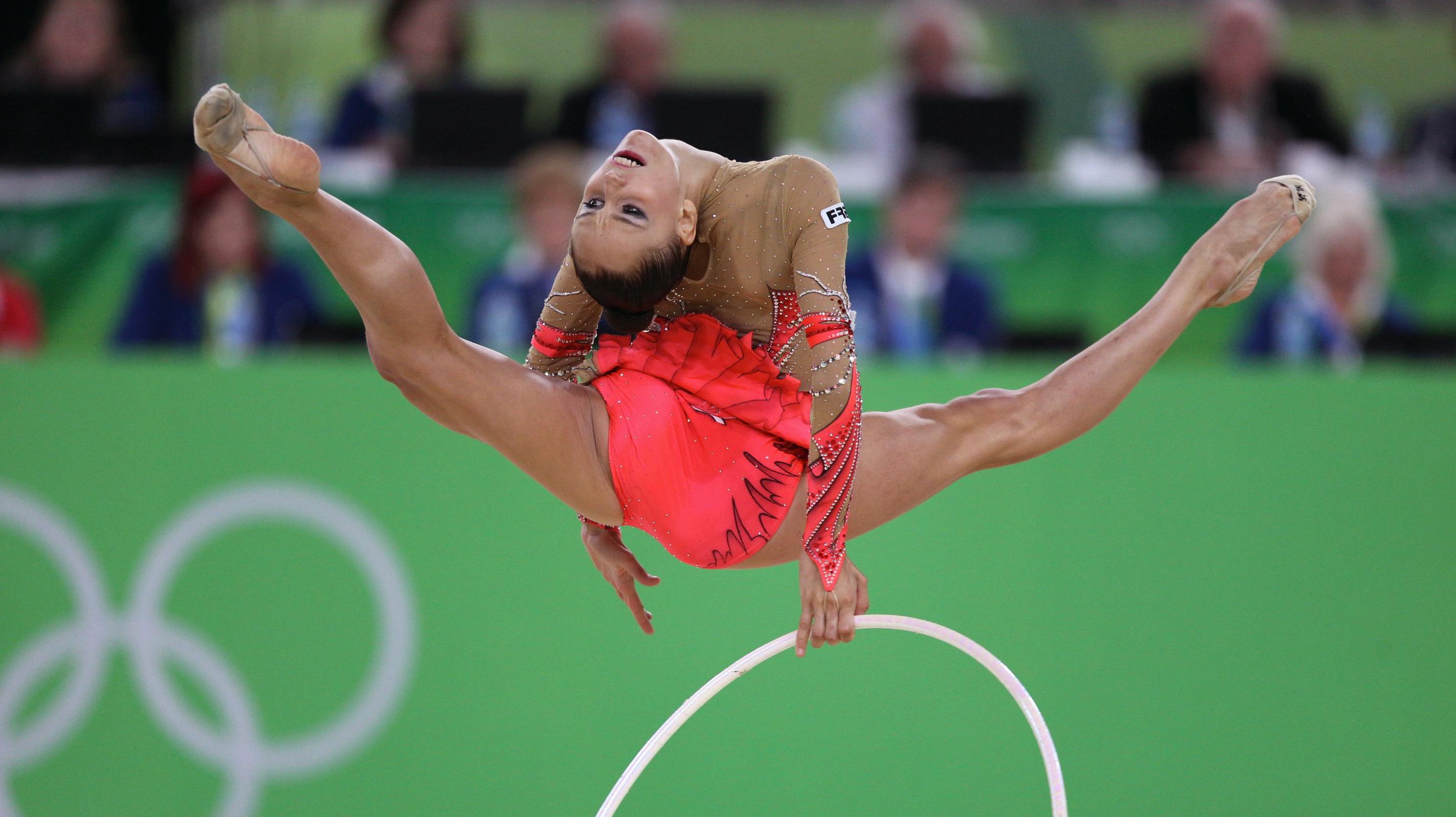 Athlete jumping in the air in a competition, doing the split while bending backwards in the air and looking backwards.