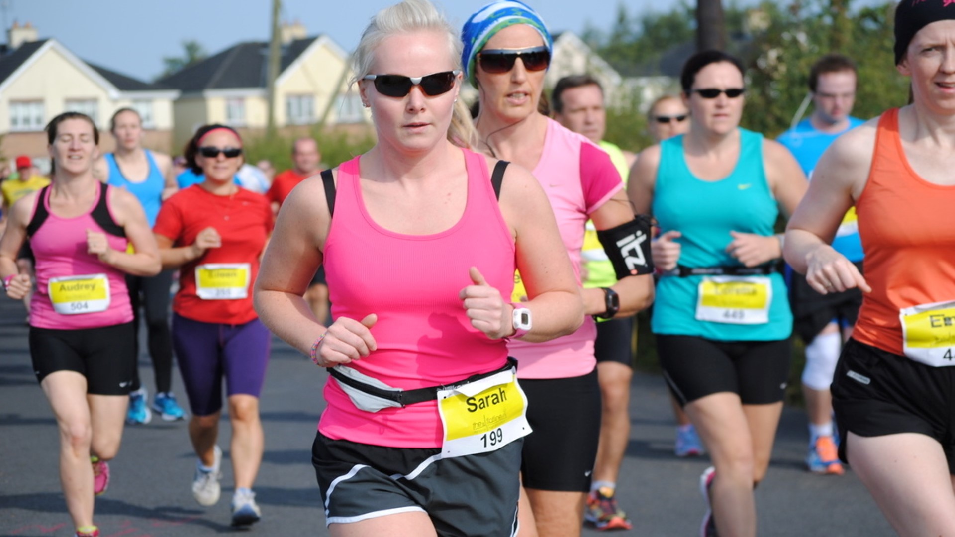 Several recreational runners in a race seen from the front. Many with their bib numbers visable. 