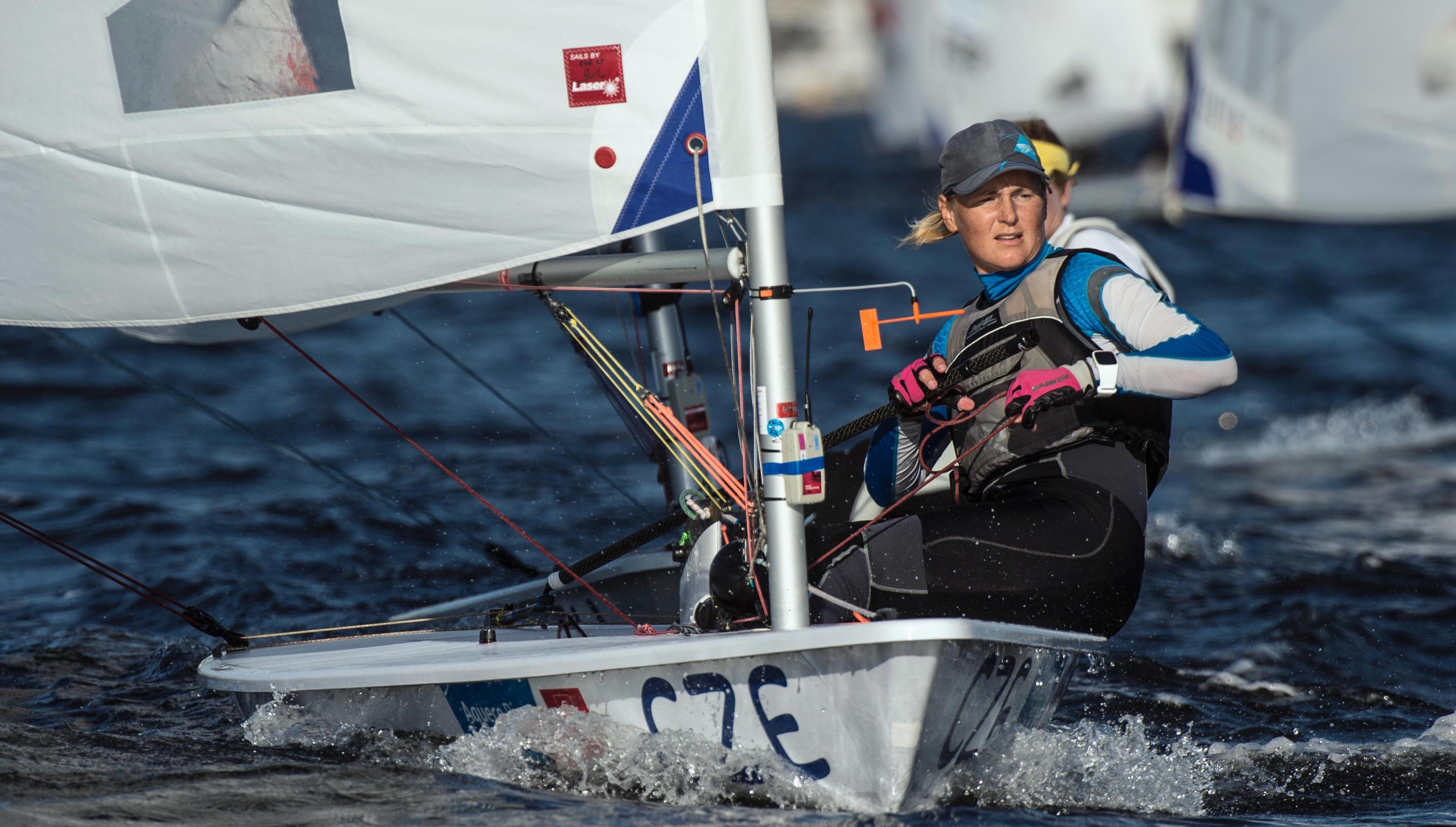 Sailor in a competition, sits in the side of the boat, looking forward.