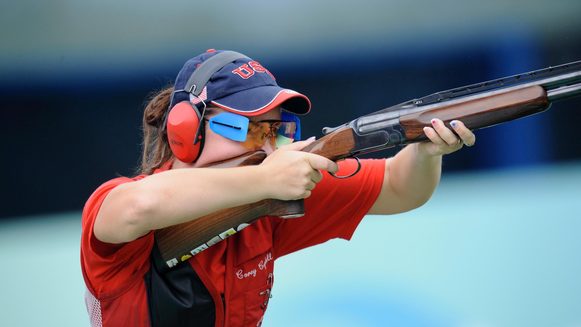 Athlete with a shotgun, holding it up to her face, aiming, getting ready to shoot.