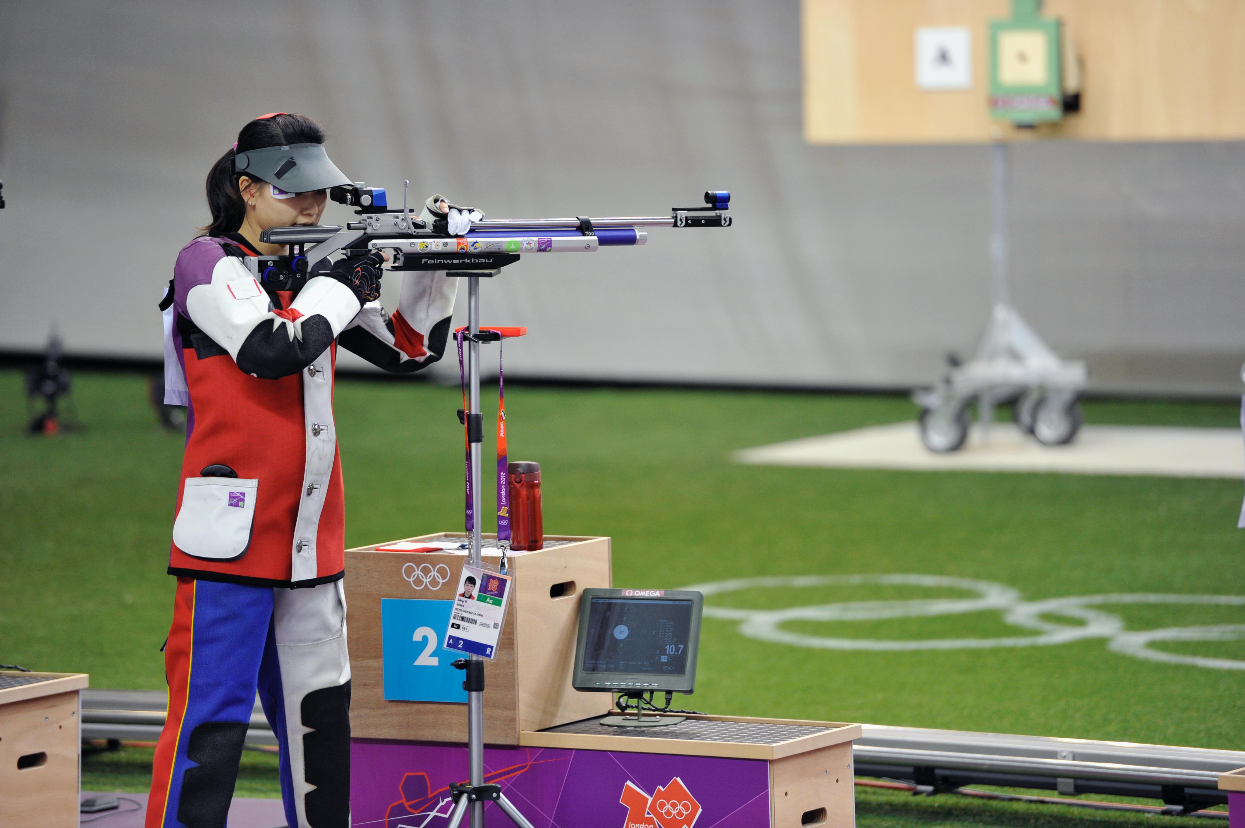 Athlete in a competition, aiming with her rifle that is supported by a stand.