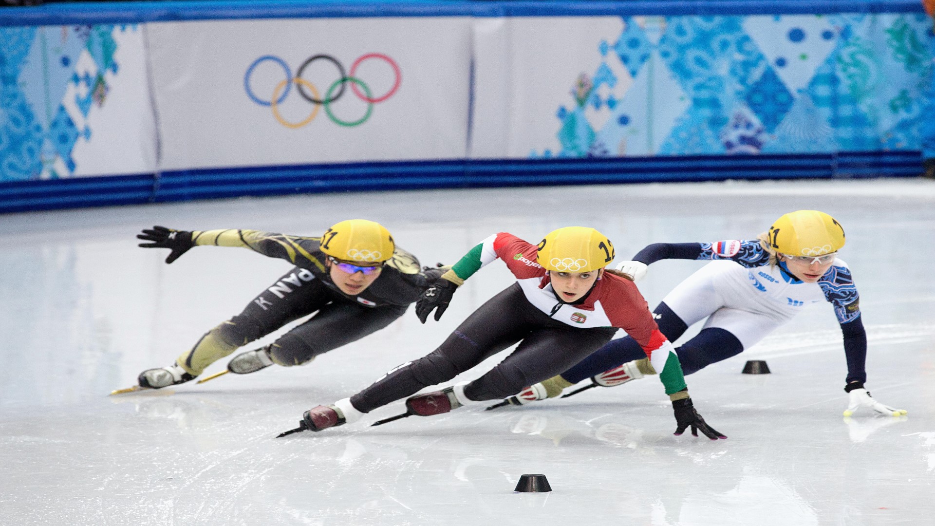 Three short track speed skaters in a competition on the ice, in a turn, some have their hand on the ice.