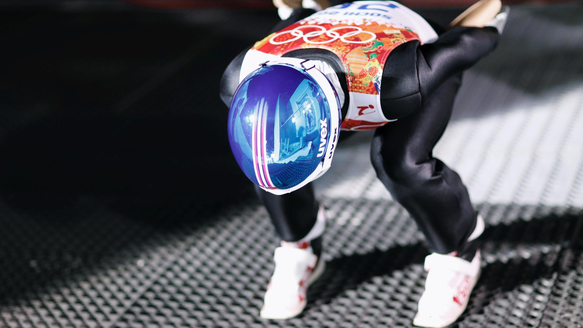 Athlete standing on two legs, knees bendt, with full skijumping suit and helmet on, practicing the take-off.