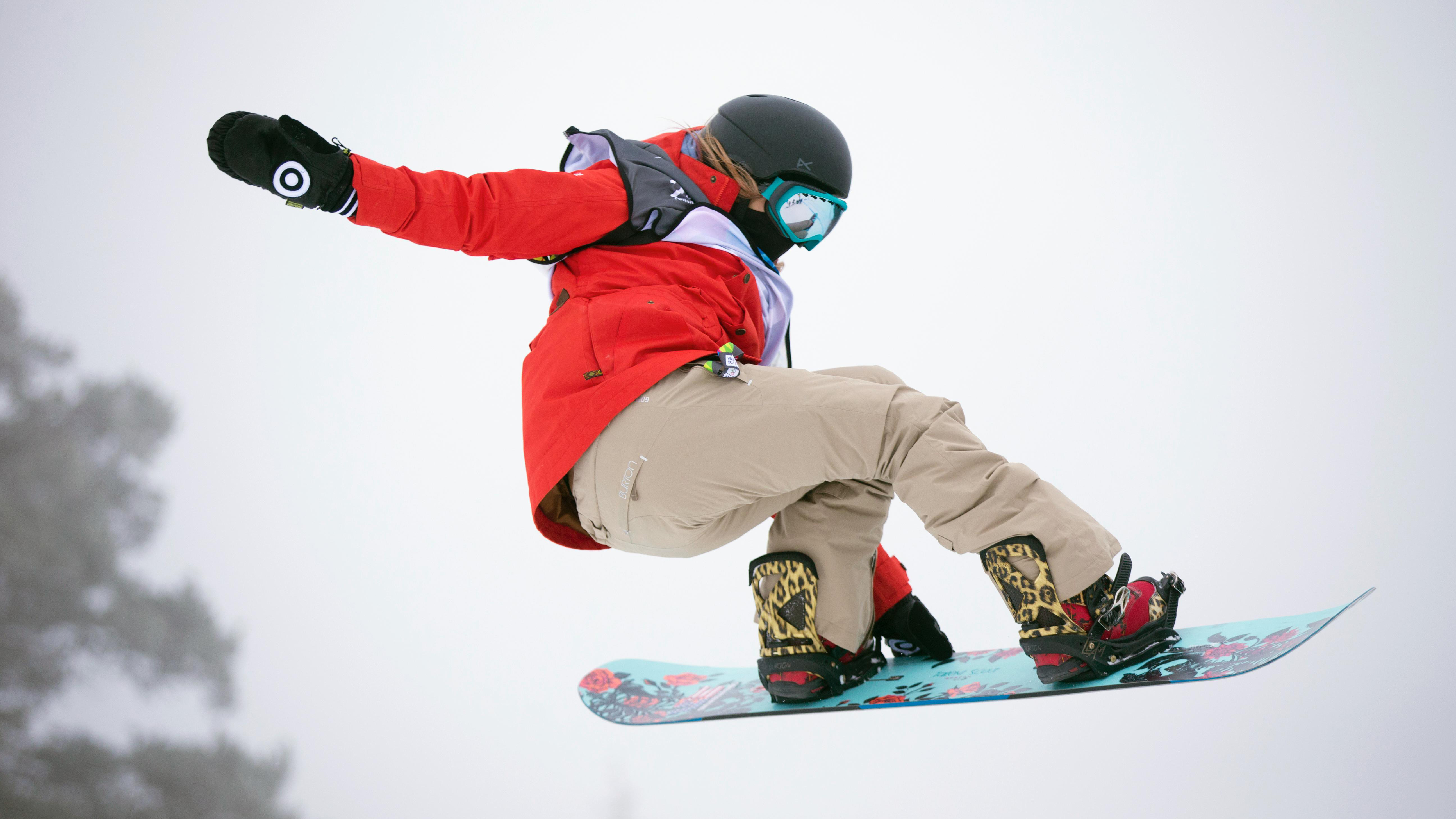 Snowboarder in the air, left hand on the board, body tilted a little backwards.