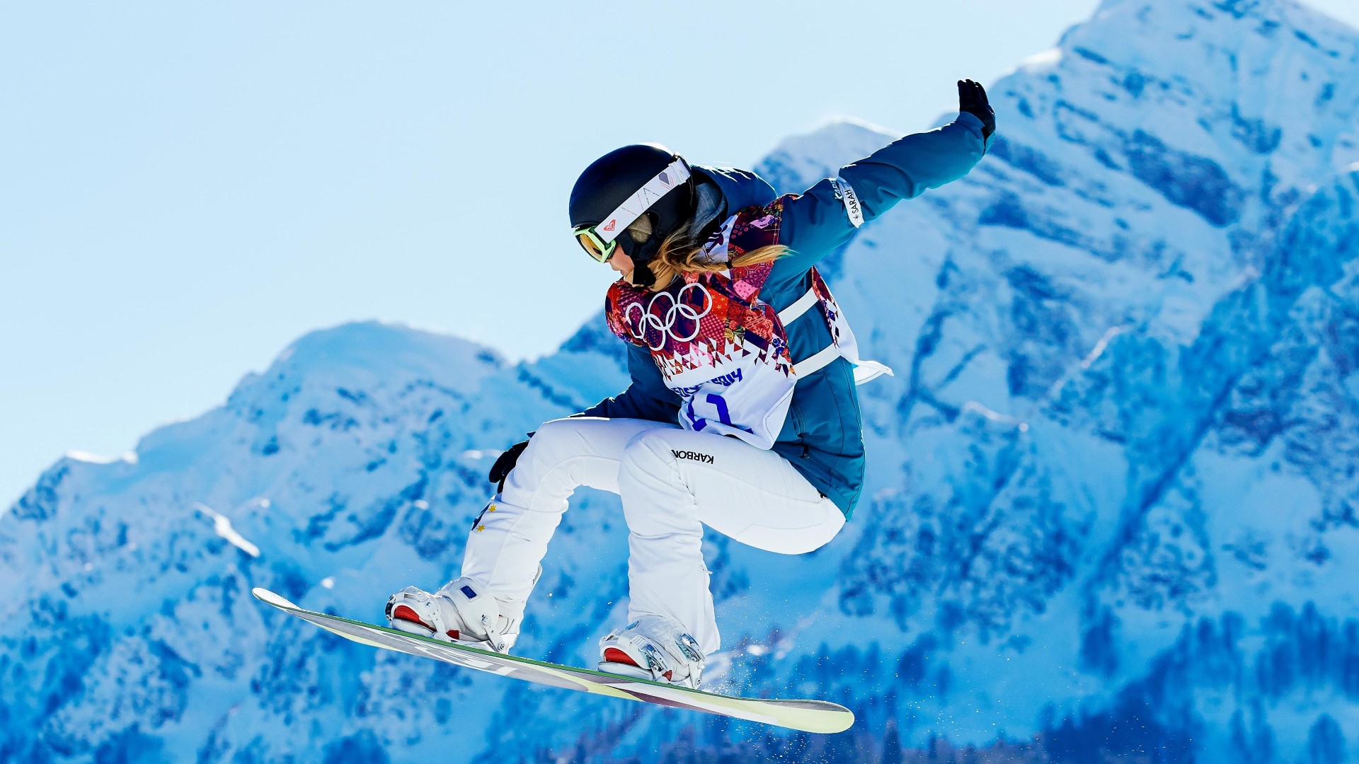 Snowboarder in the air during a competition, mountains in the background.