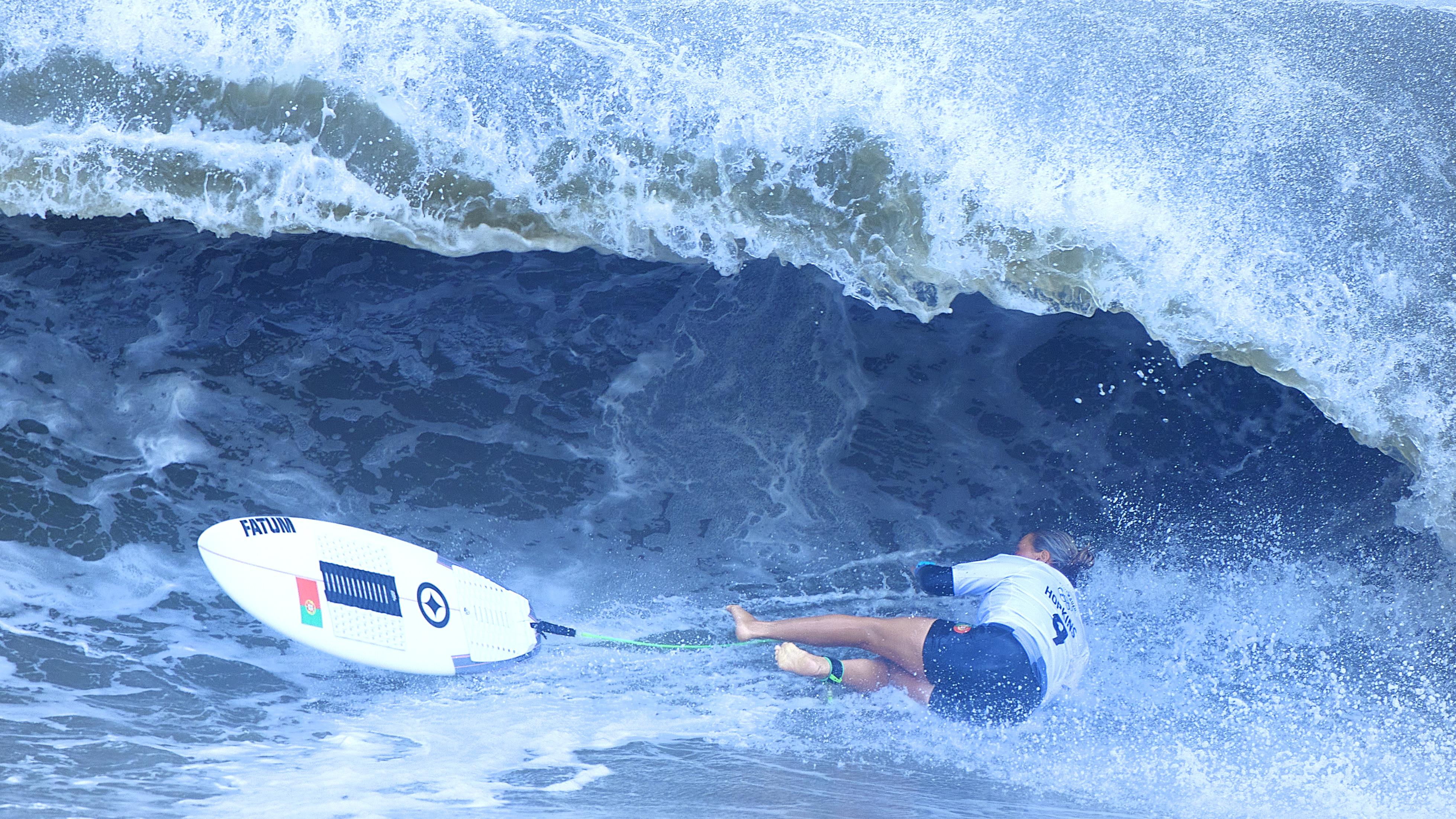 Athlete in the water, surfboard on the left, while athlete has fallen off and are landing in the water, sideways.