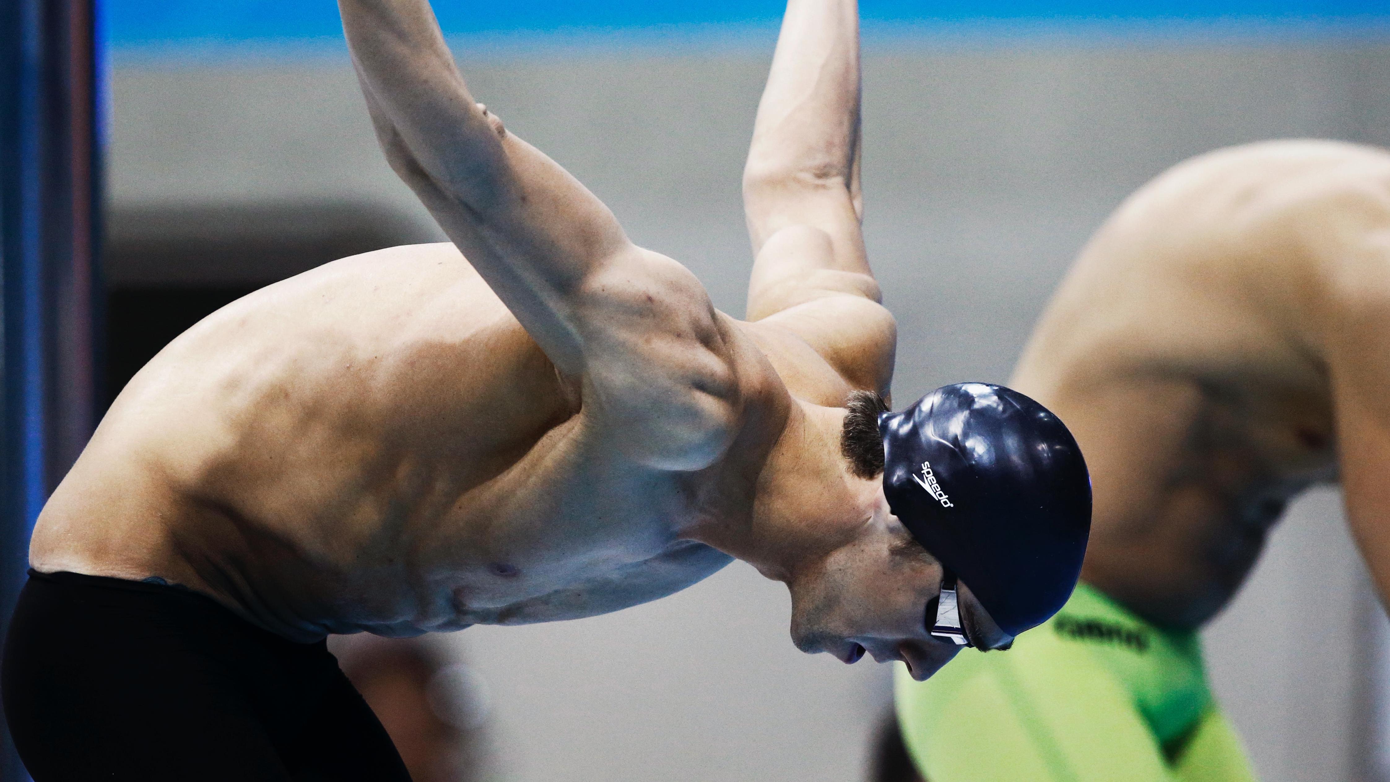 Athlete getting ready to jump into the pool, he is bendt forward, hands straight and backwards.
