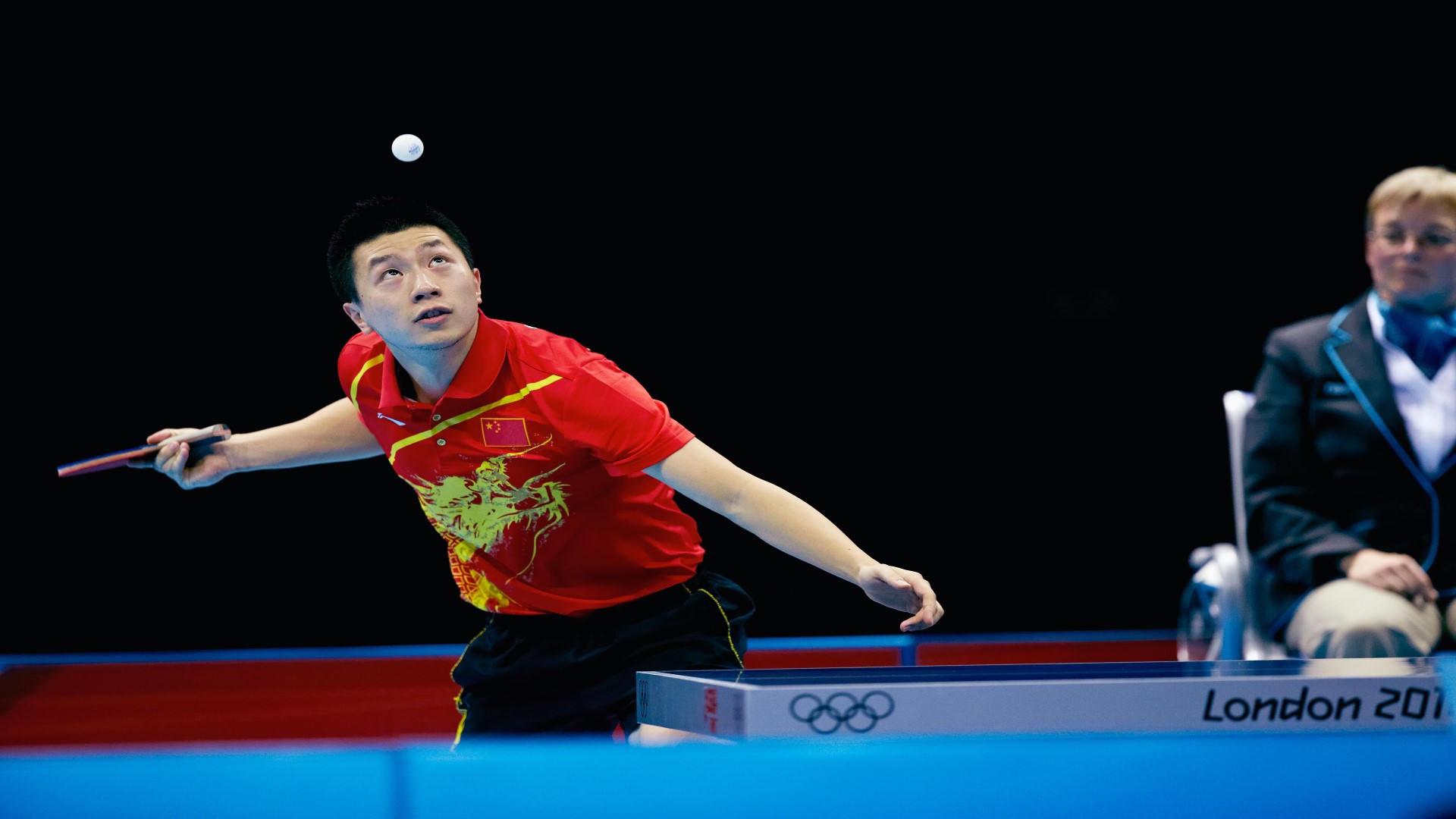 Athlete getting ready to serve, the ball is in the air, athlete looking up on the ball, racket in his right hand.