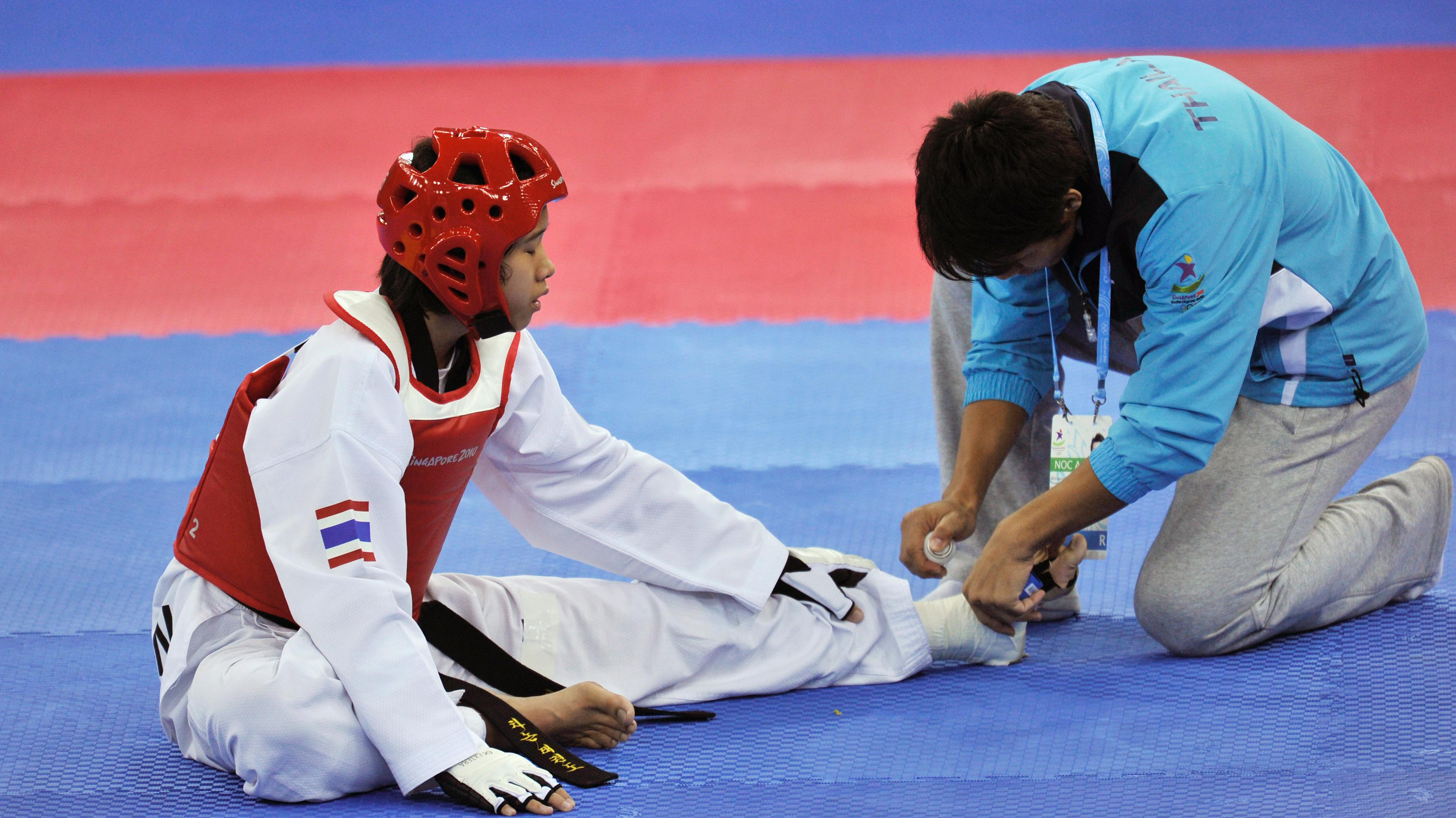 Athlete sitting on the ground getting her ankle taped by a medical professional.