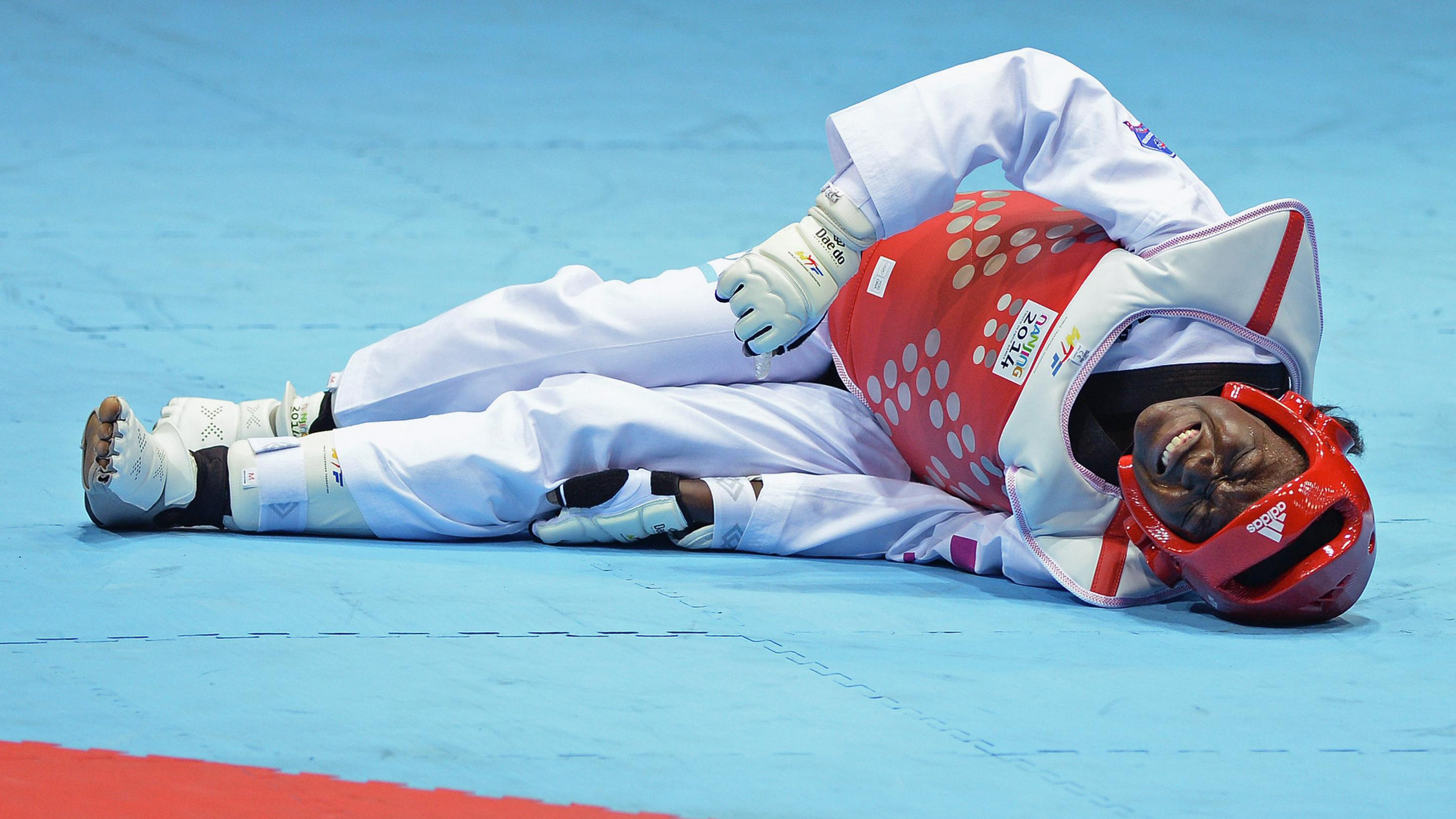 Athlete lying on the ground, in pain, holding her left hand on the left side of the knee.