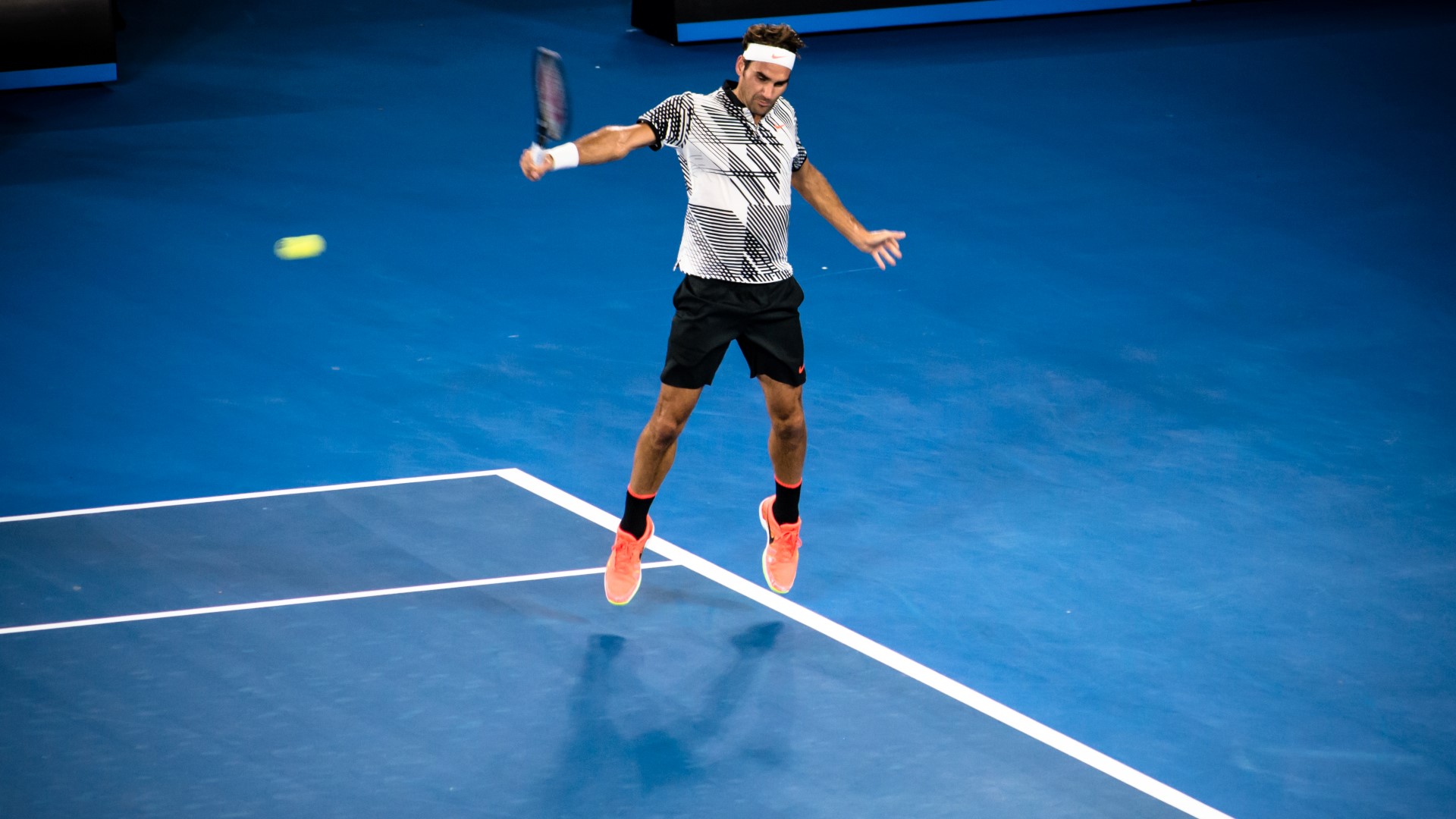 Athlete on the tennis court, in the air, having just hit the ball with his racket.