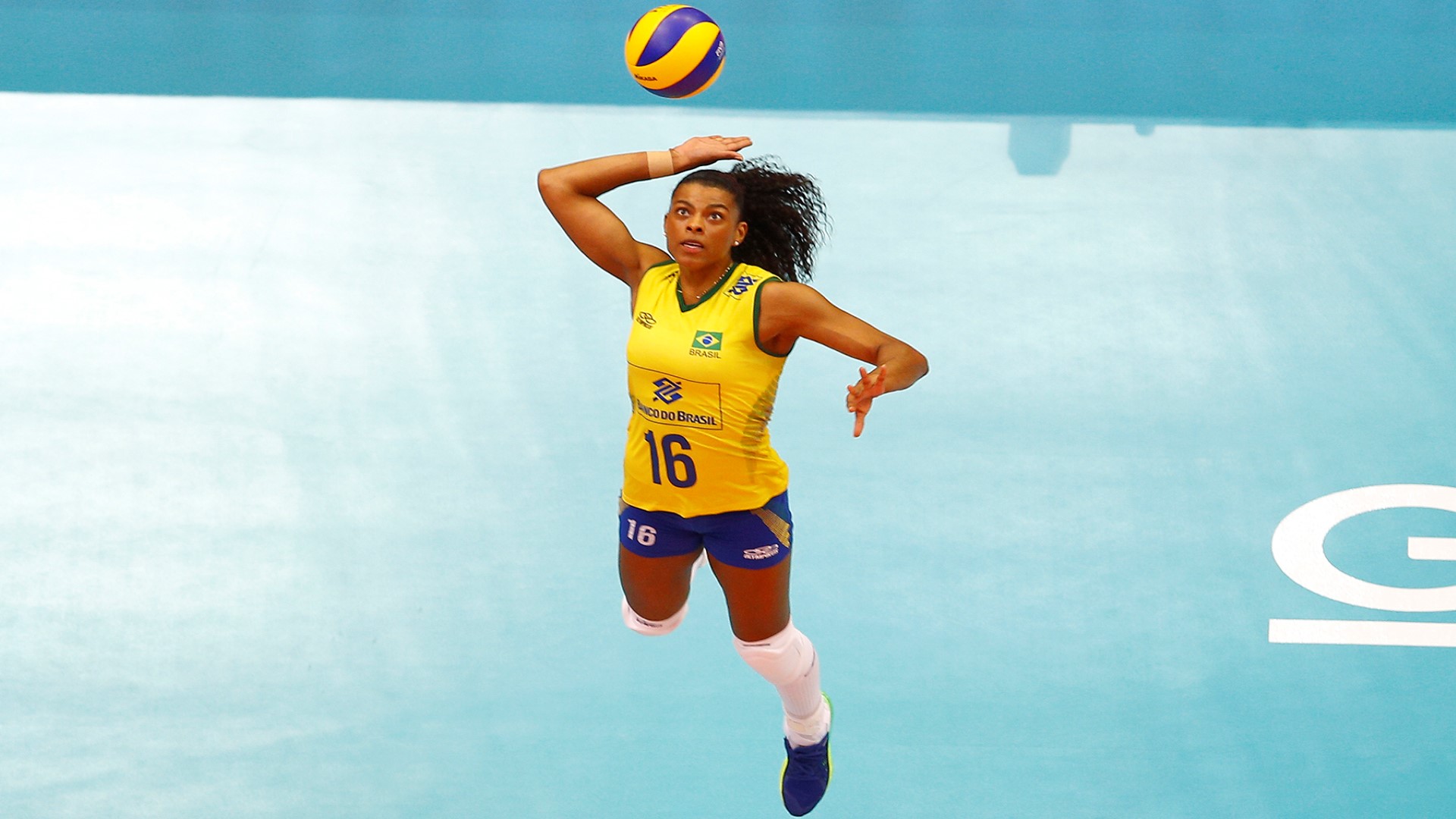 Volleyballplayer jumping up in the air, eyes on the ball in the air, right hand high up, getting ready so serve the ball.