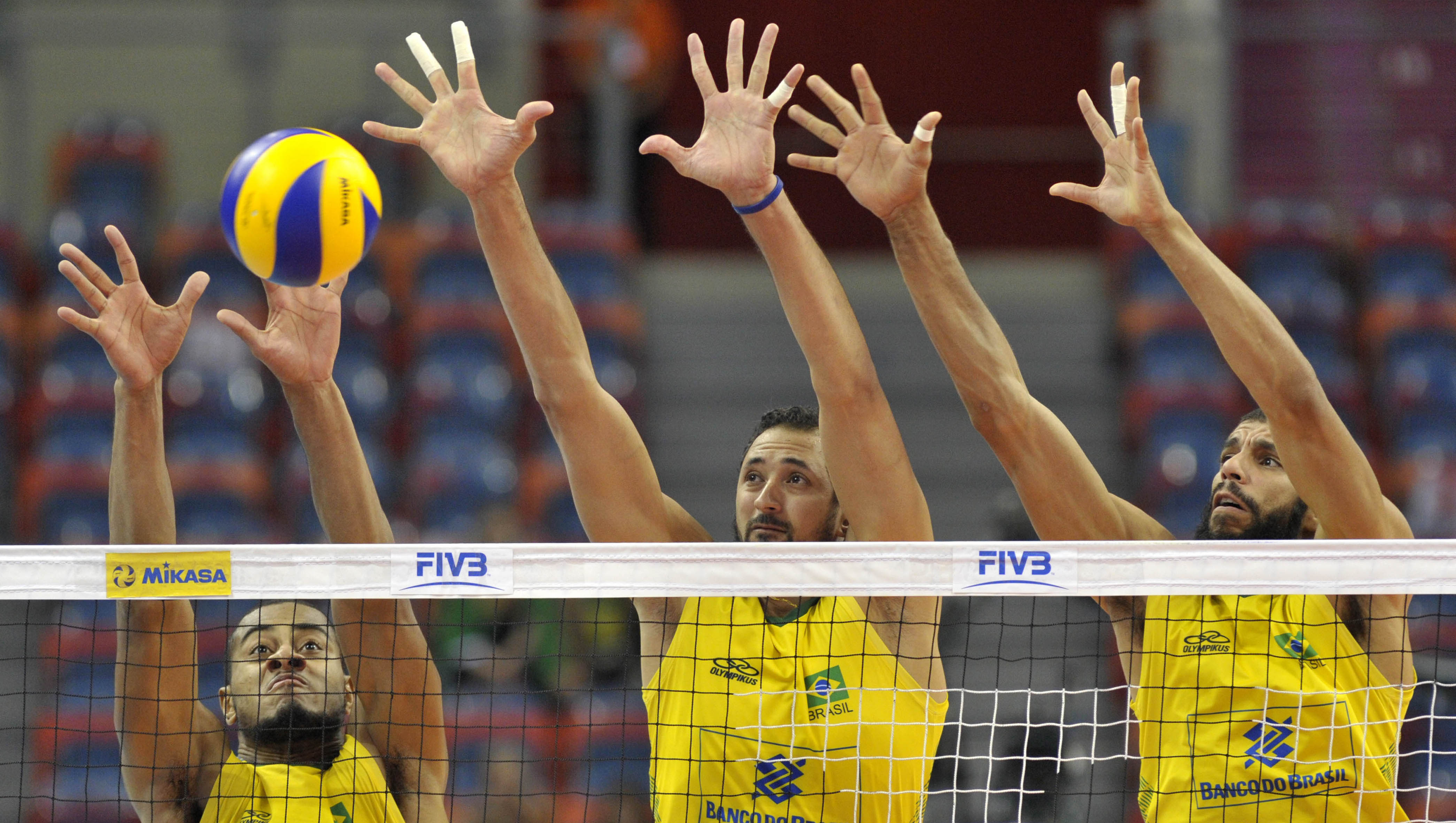 Three players on the same team trying to block a ball by the net.