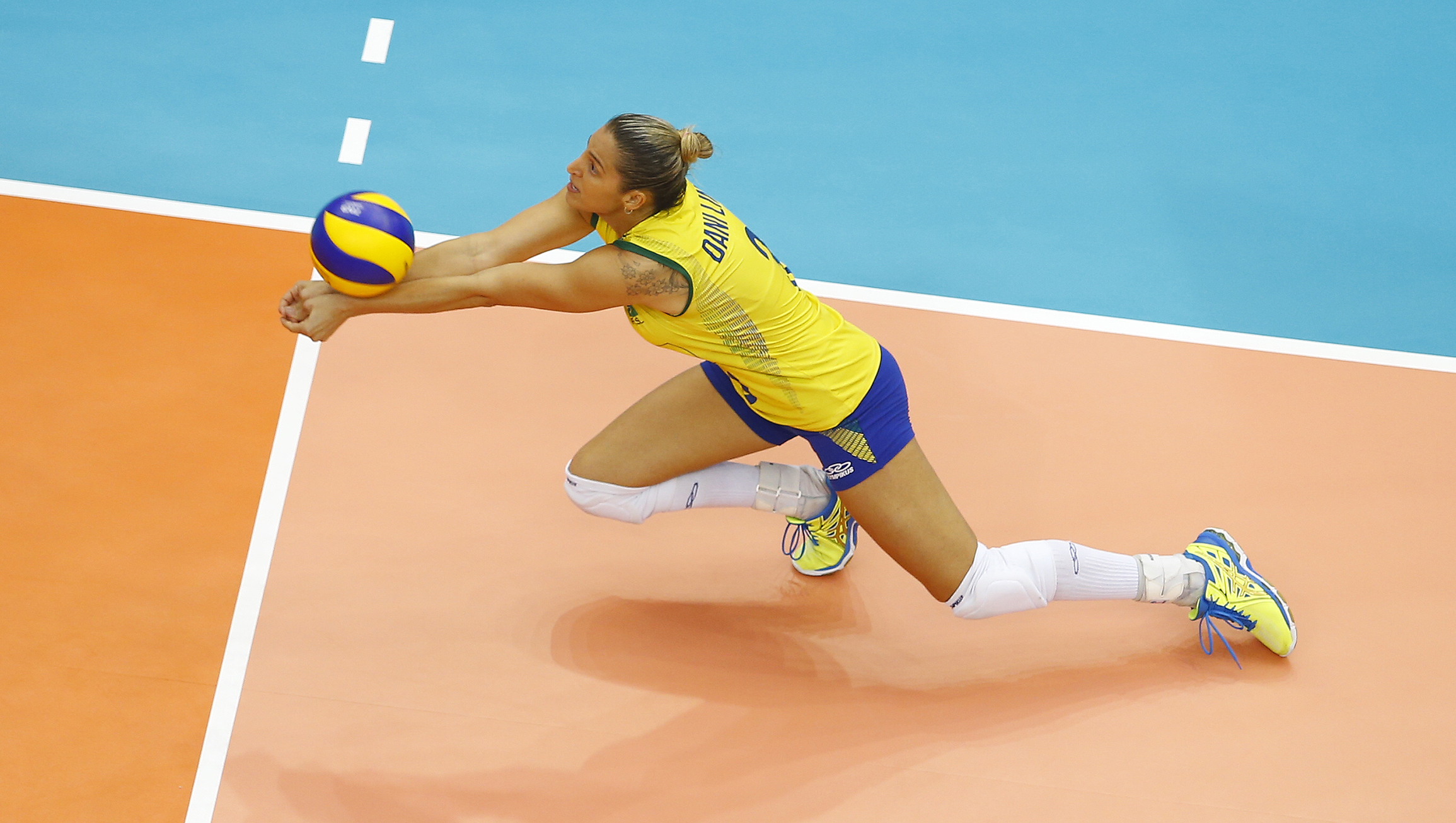 Volleyballplayers in the court, throwing herself forward to catch the ball with both her hands together.