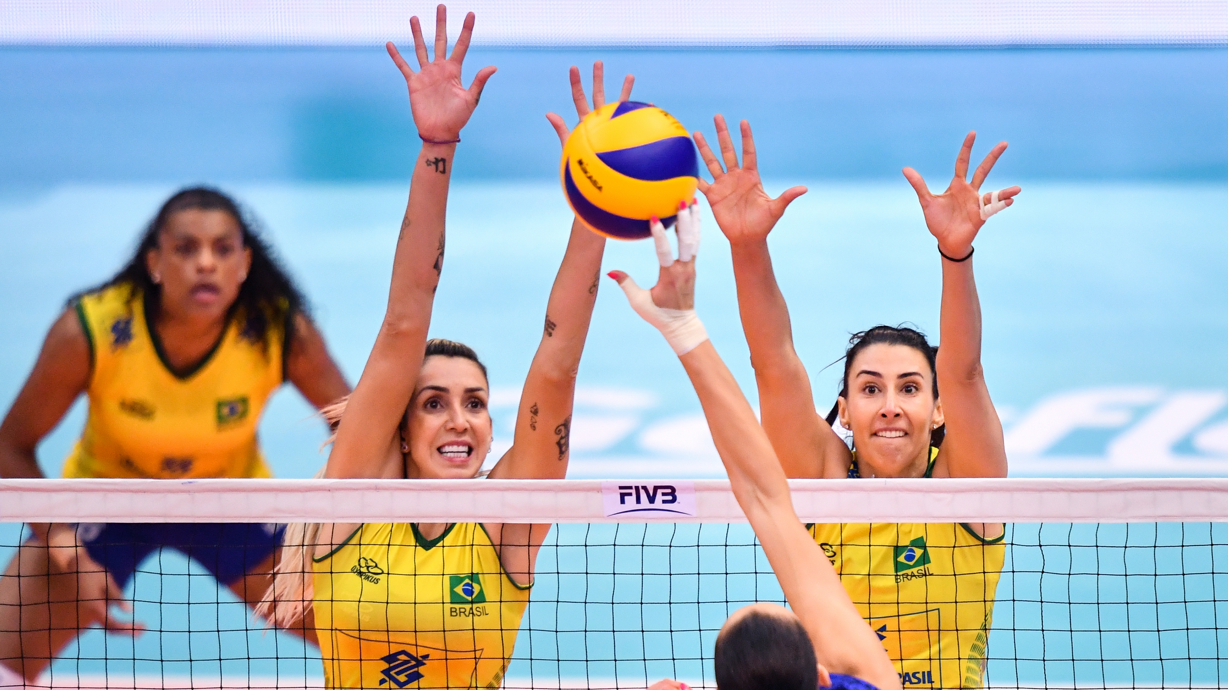 Two volleyballplayers trying to block another players ball along the net.