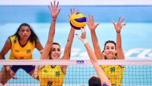 Two volleyballplayers trying to block another players ball along the net.