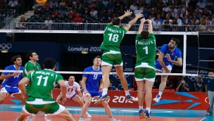Volleyball match, where to players are tring to block the ball at the net from an opponent on the other side of the net who have just smashed the ball.