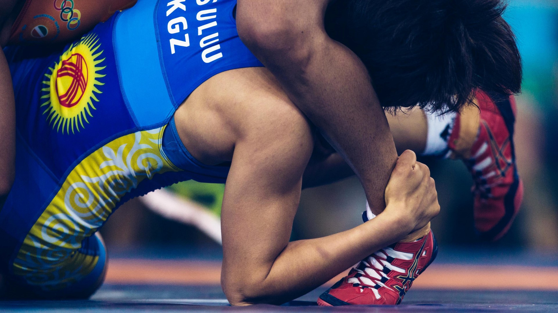Two wrestlers on the court, clos up. One holding around the ankle of the other athlete.